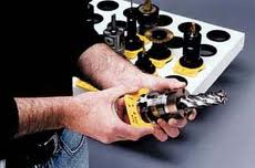 A person's hands hold a yellow and black Snap-on tool over a gray workbench with tools on a nearby white tray.