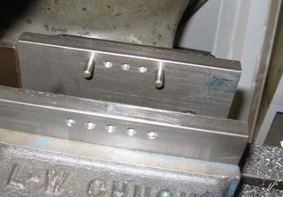 Metal workpiece with rectangular shape and three evenly spaced holes along its top edge, on a metal surface.