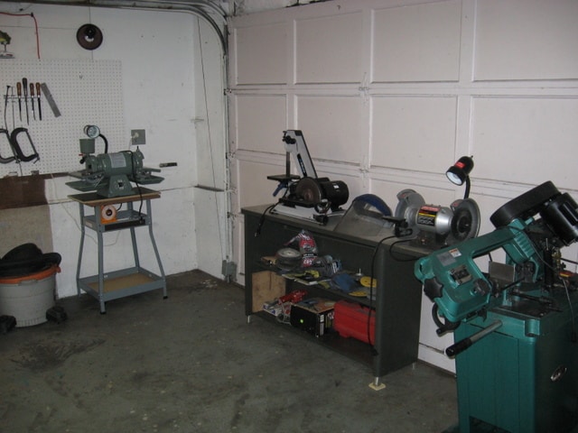 Well-organized garage workshop with tools, bandsaw, drill press, and metalworking machinery.