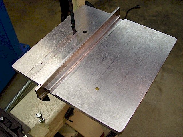 Silver metal fence on a band saw with flat top surface and rounded corners.