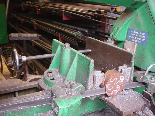 Metalworking machine with vise and attached bandsaw and jack screw on a workshop background.