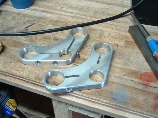 A metal part with 2 holes and a central slot, on a wooden workbench.