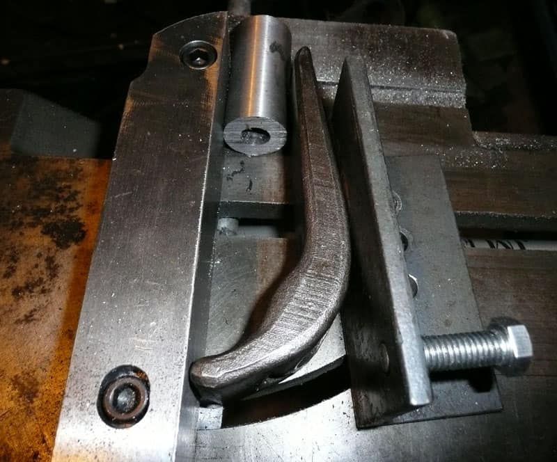 Metalworking clamp with curved jaw on machine shop bed.