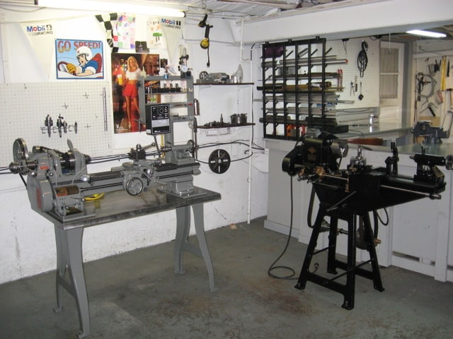 Well-organized workshop with two lathes and various tools on white walls and a concrete floor.