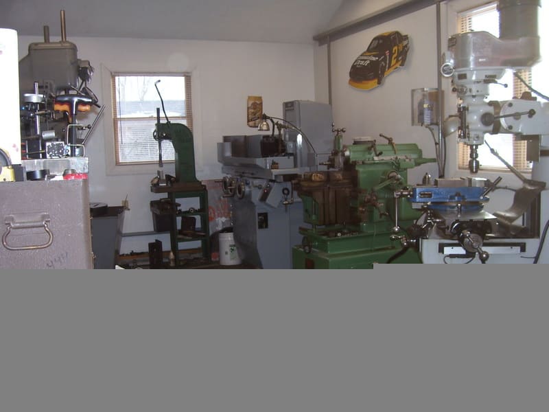 A compact garage or workshop with heavy-duty machinery and natural light from two windows.