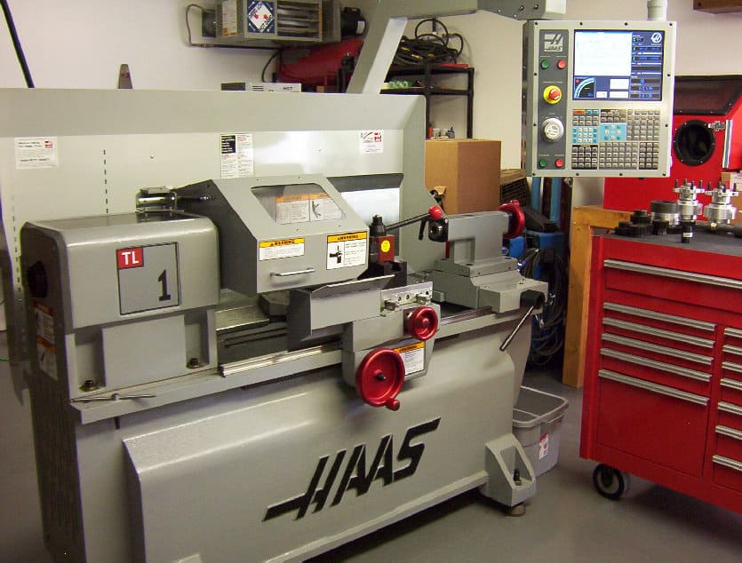 Haas TL-1 Turning Lathe in a well-lit workshop setting with gray metal components, red and black accents, and HAAS logo.