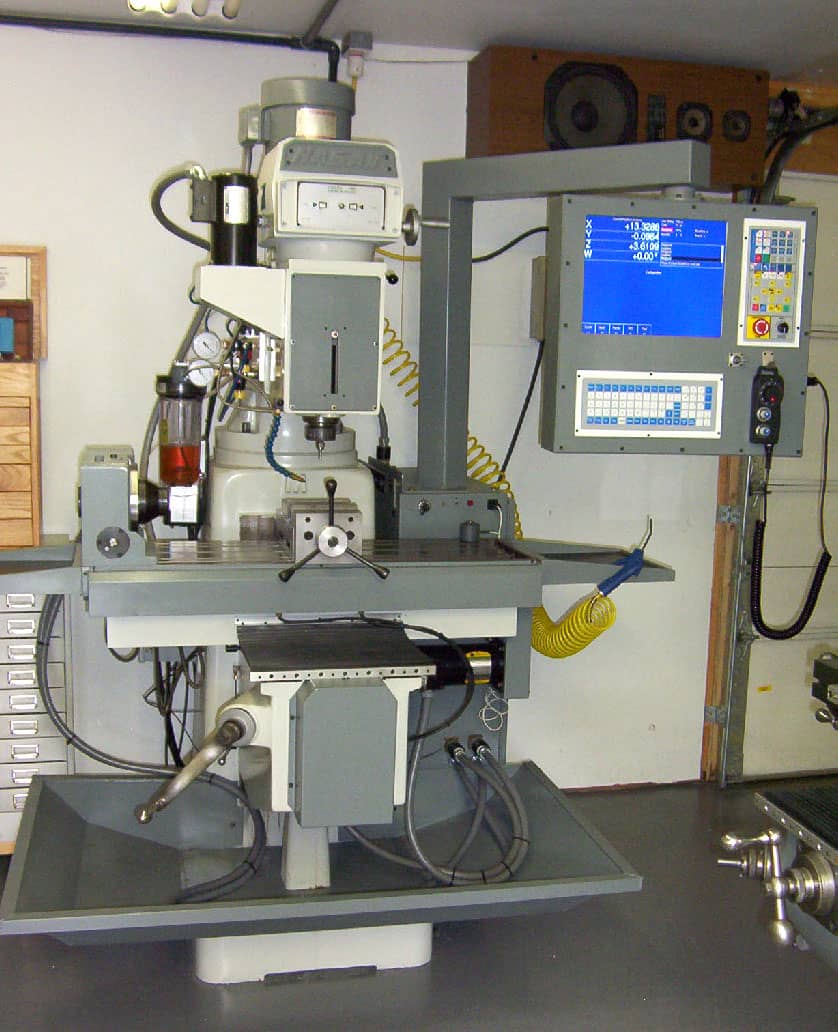 Grey CNC milling machine with control panel and yellow coiled tube in a factory workshop.