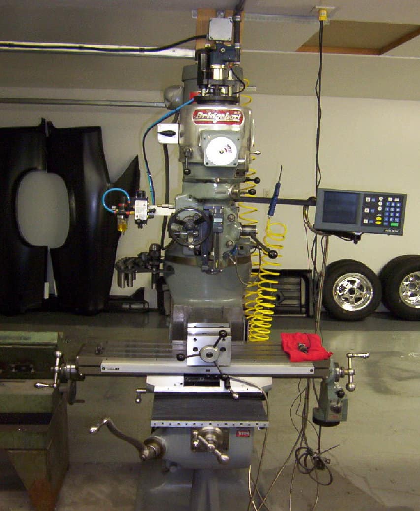 Industrial milling machine in workshop or factory setting surrounded by machinery and equipment on a concrete floor.