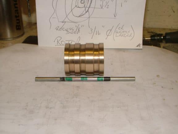 A cylindrical brass or bronze object with a silver rod.