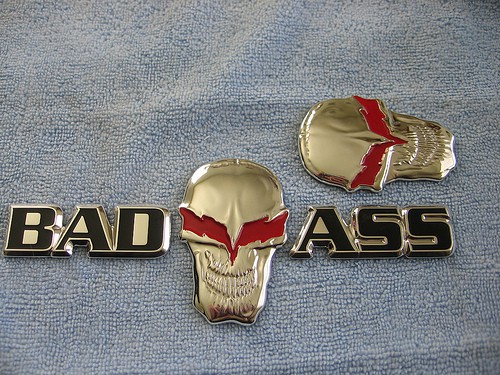 Gold skull with red eyes and black "BAD ASS" text on gray background.