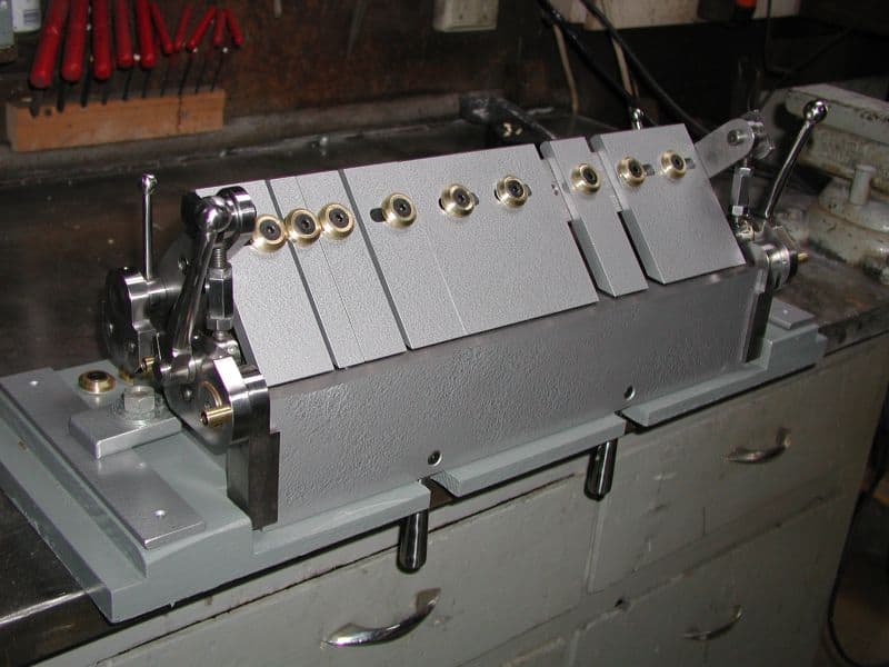 A metalworking machine with brass knobs and handles on a gray base plate in a workshop setting.