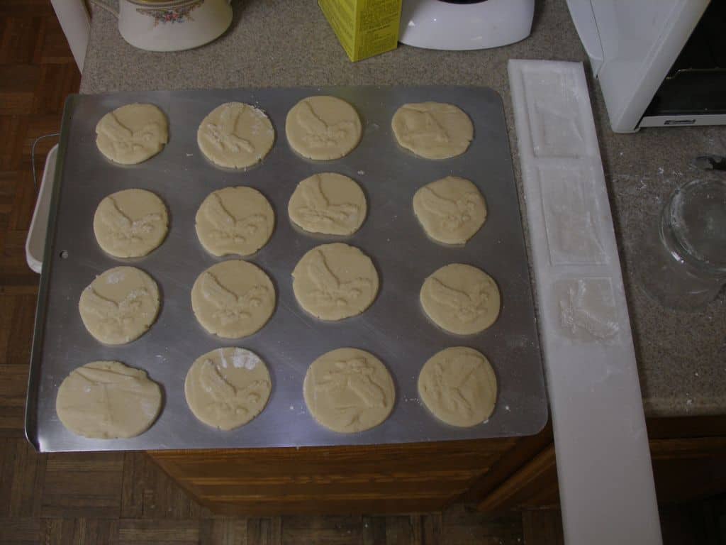 Stainless steel baking sheet with rows of cookies featuring embossed bird in flight designs.