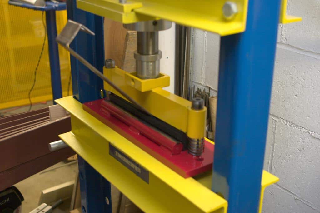 Yellow and blue metal press with a red base, featuring a large metal rod.
