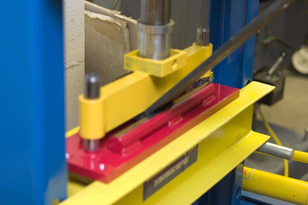 Heavy-duty press with yellow arms and red base in a workshop.