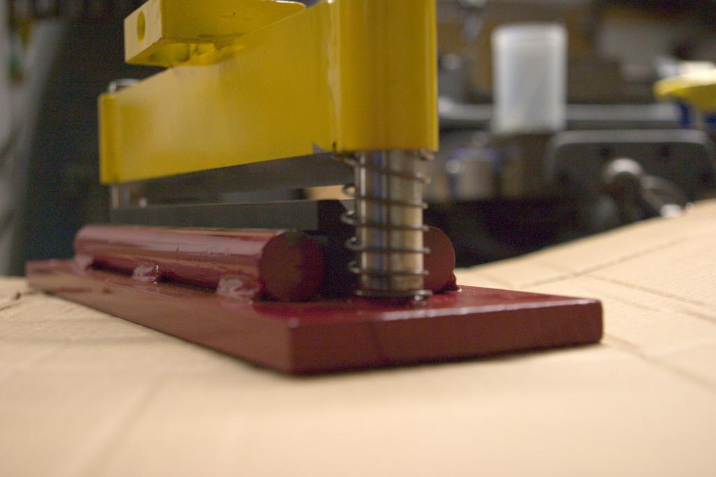 Yellow metal tool with spring-loaded mechanism on light-colored surface.