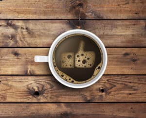 A white coffee cup filled with dark brown liquid on a wooden surface.