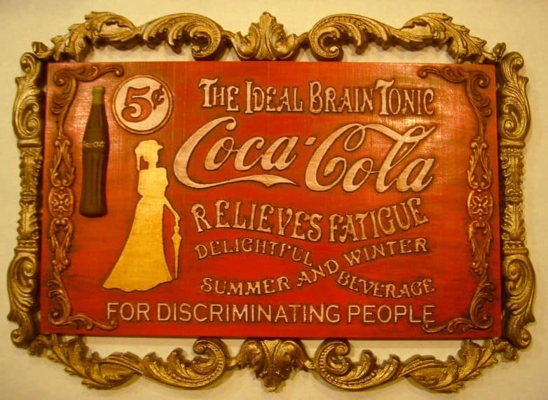 A vintage Coca-Cola sign with ornate gold frame and iconic logo.