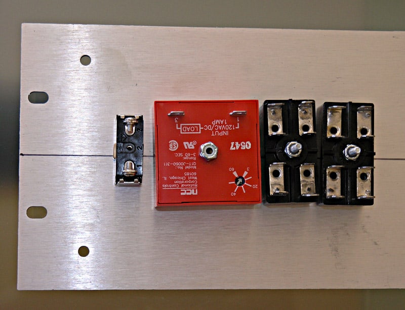 Metal plate with holes and components including relay switch, metal piece, and black component.