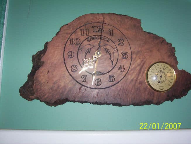 A wooden driftwood clock with a dolphin design, decorated with a compass rose and intricate wood burning details.