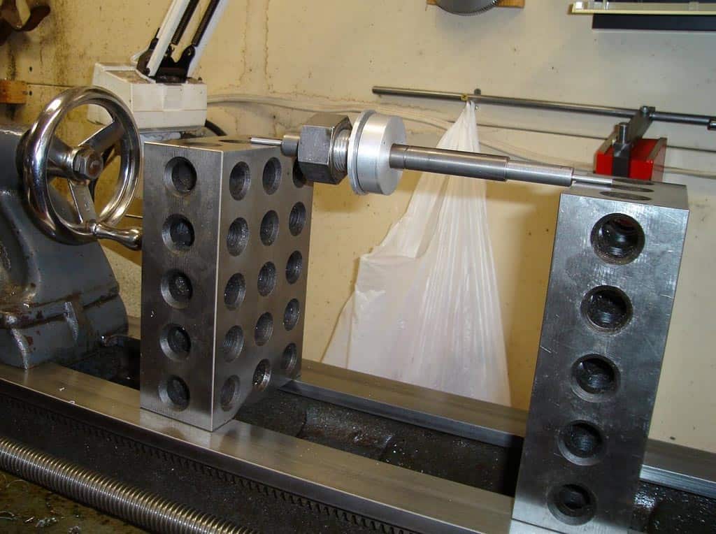 A metal lathe setup with a workpiece featuring longitudinal holes and various tools and attachments in the background.