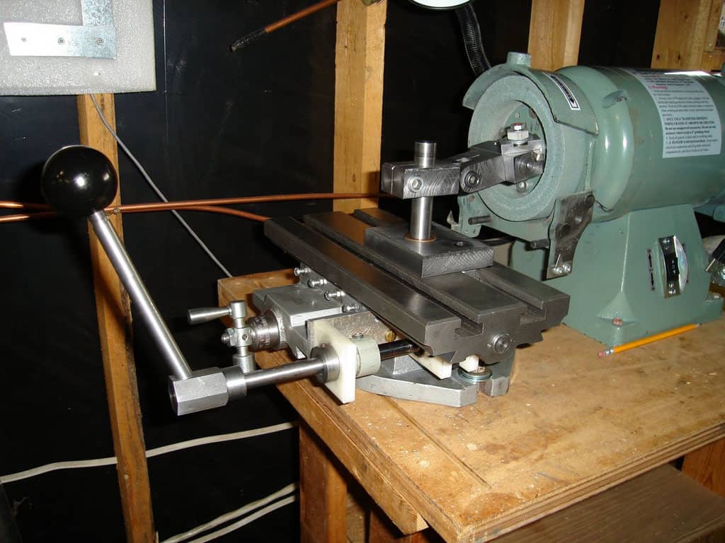 Old-fashioned lathe with wooden table and metal components on a dark background.