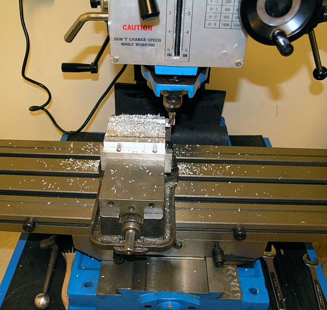 A milling machine with various tools and accessories on a blue table with black rubber feet.