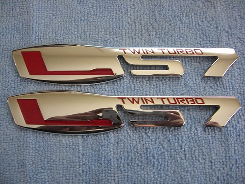 Chrome-plated LS7 Twin Turbo emblem on blue fabric.