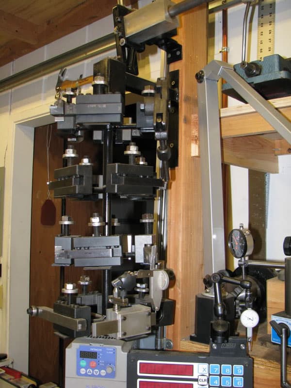 Large metal lathe tool carousel with multiple tools, each with a white handle, arranged in a vertical column.