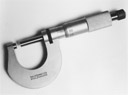 Silver micrometer with black handle and curved jaw on light gray background.