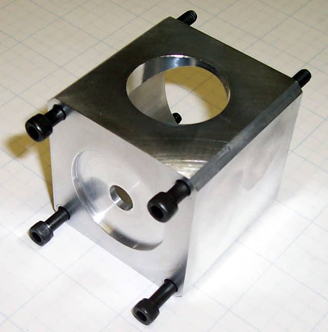 Metal block with hole and black screws.