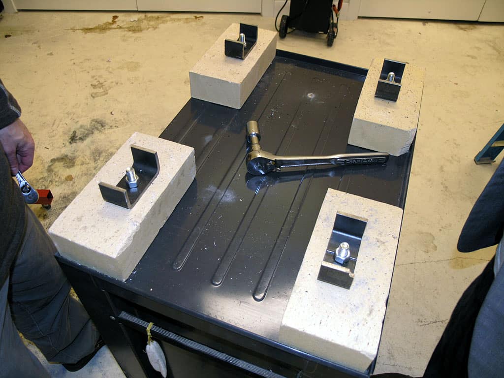 Black metal table with four white blocks holding metal brackets in a garage or workshop.