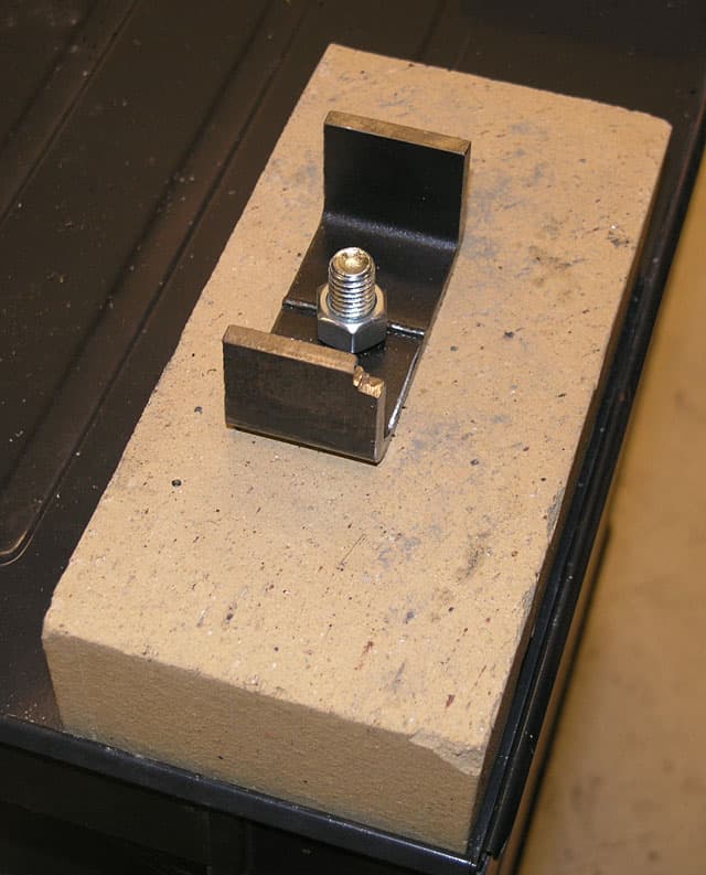 Tan-colored material block with metal bracket, square nut, and bolt.