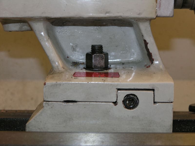 Metalworking machine base with black bolt and red label on light gray metal.