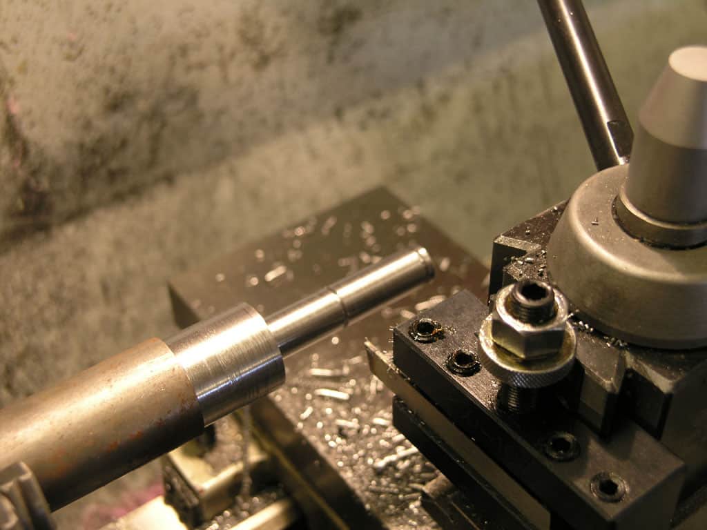 Metal rod being machined on a lathe in a well-lit workshop.