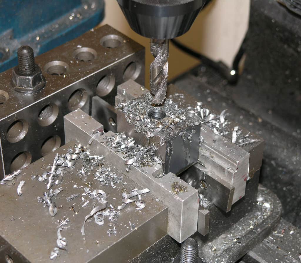 Metalworking operation: milling or drilling on aluminum with drill bit and metal shavings.