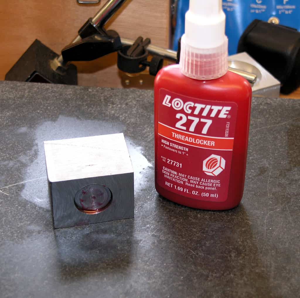 A red bottle of Loctite 277 threadlocker with orange label on a workbench among various tools.