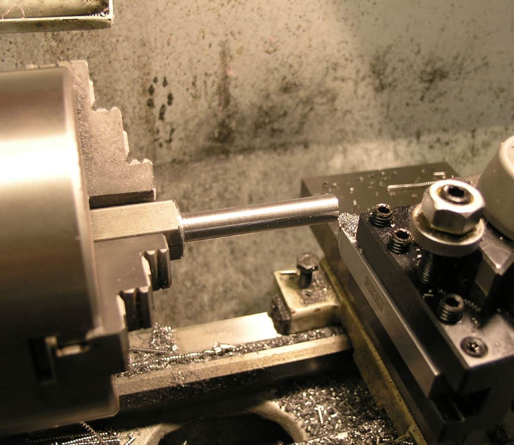 Metalworking lathe in a workshop setting with a machined metal rod on its bed.