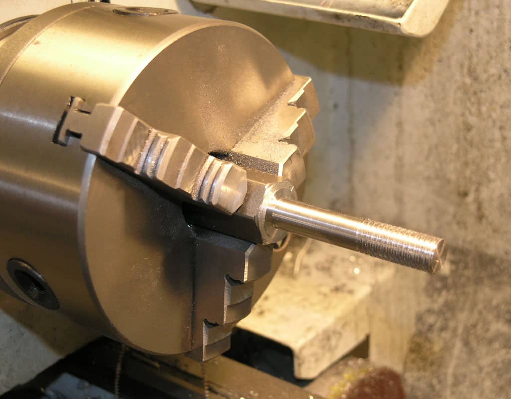 Metalworking lathe chuck with radial jaws and threaded rod.