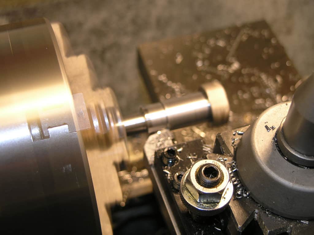 Metalworking lathe in operation, with metal components and cutting tool engaged.