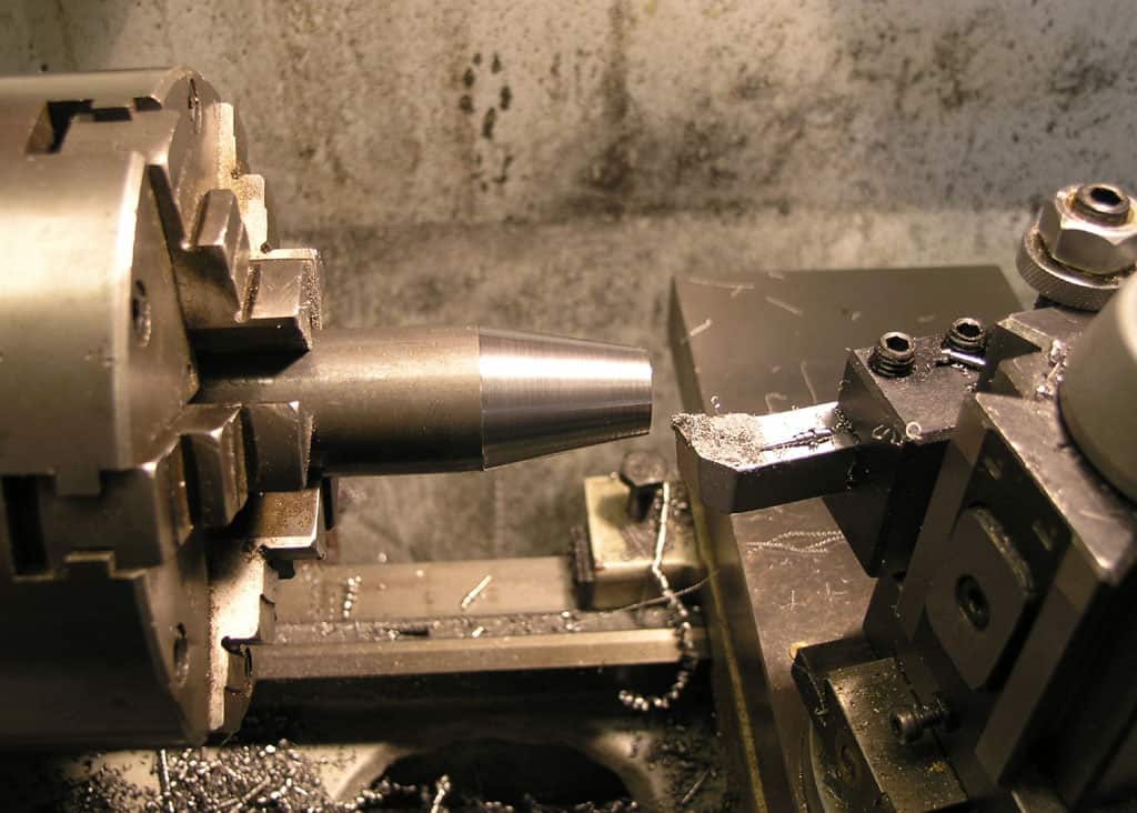 Metal object with conical shape being machined on a lathe, featuring a smooth steel surface.