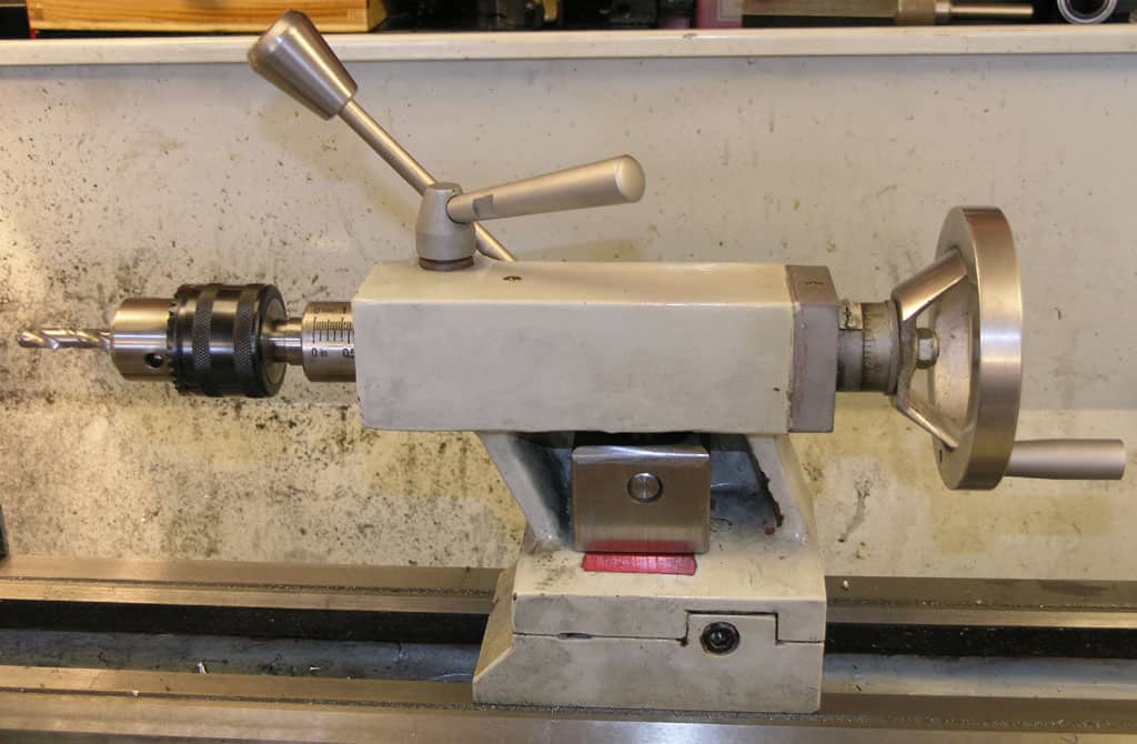 A drill press with a metal body and adjustable handle mounted on a stand, featuring a securely fastened chuck.