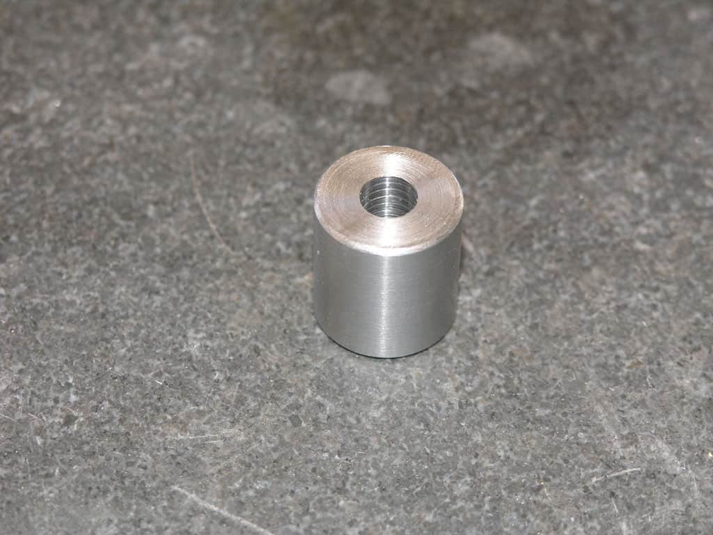 Small cylindrical metal part with threaded central hole, silver in color, possibly aluminum or steel.