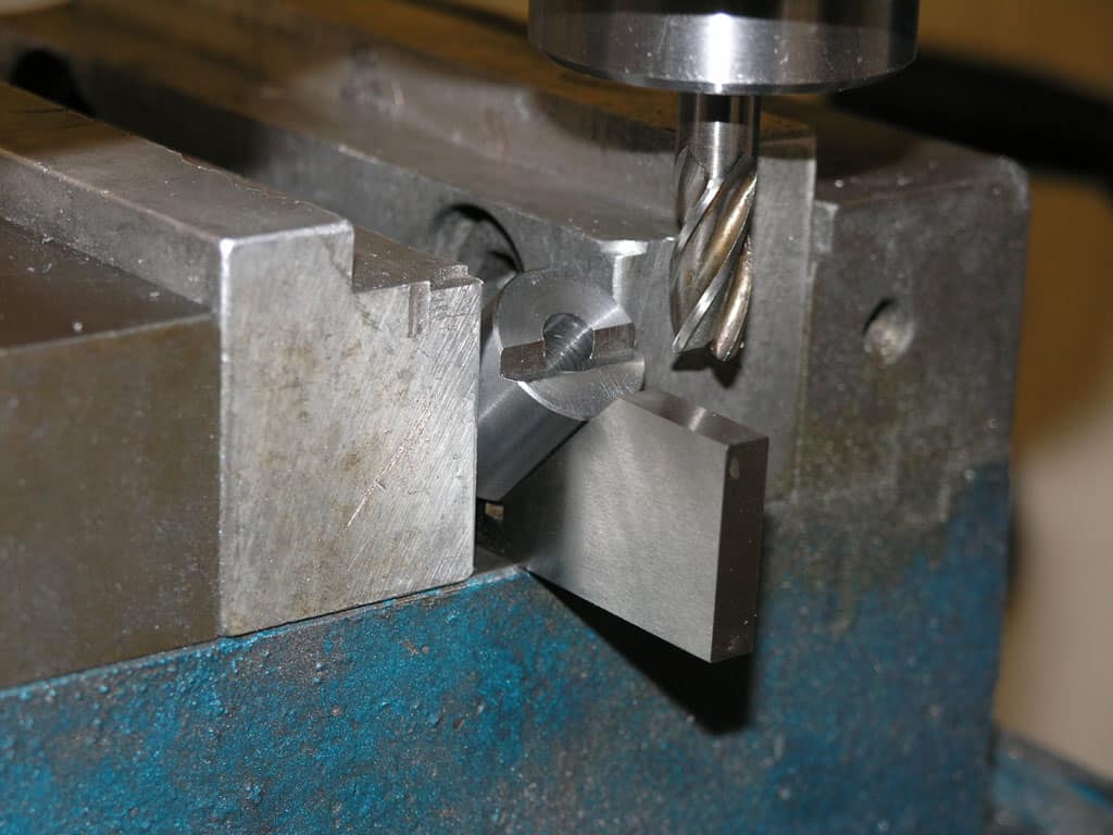 Metalworking vise holding a silver square metal piece at an angle.