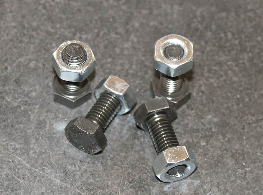 Four hex-head bolts with square nuts on a gray surface.