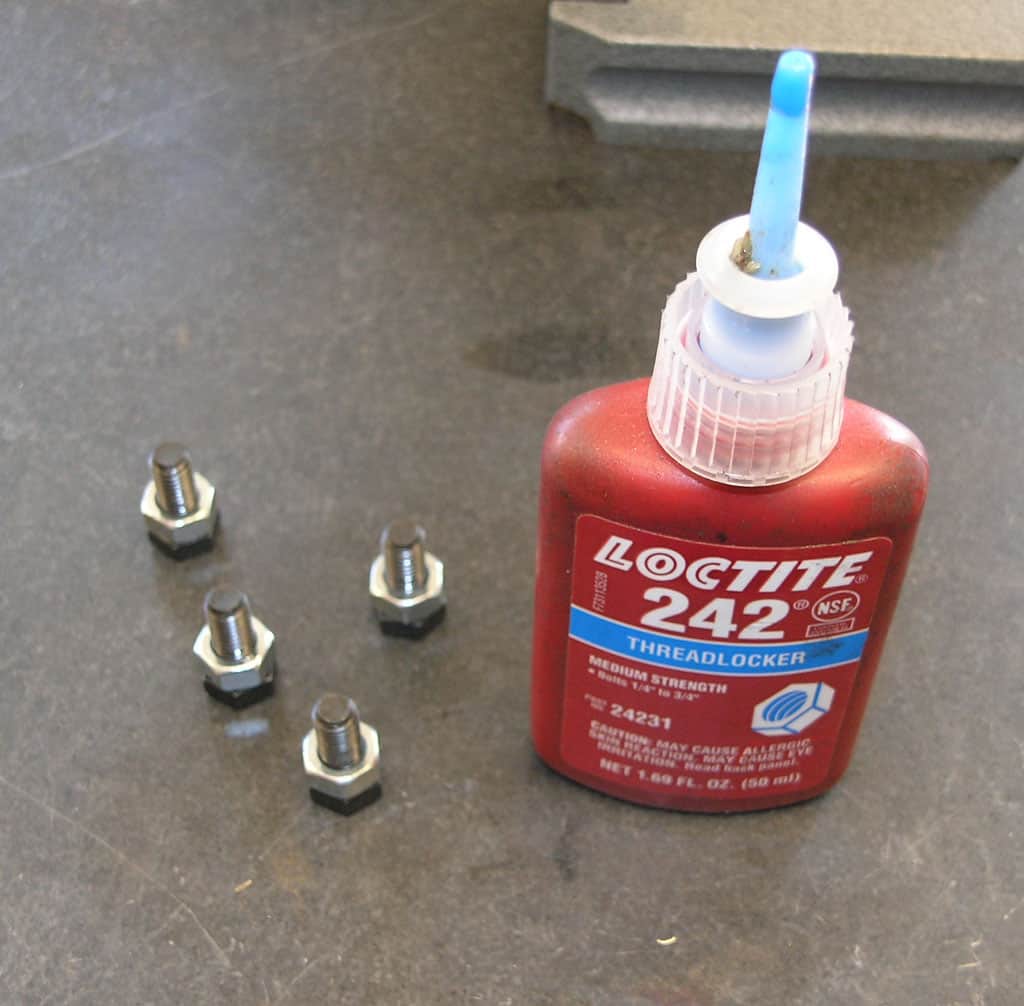 Bottle of Loctite 242 Threadlocker glue surrounded by six bolts on a gray surface.