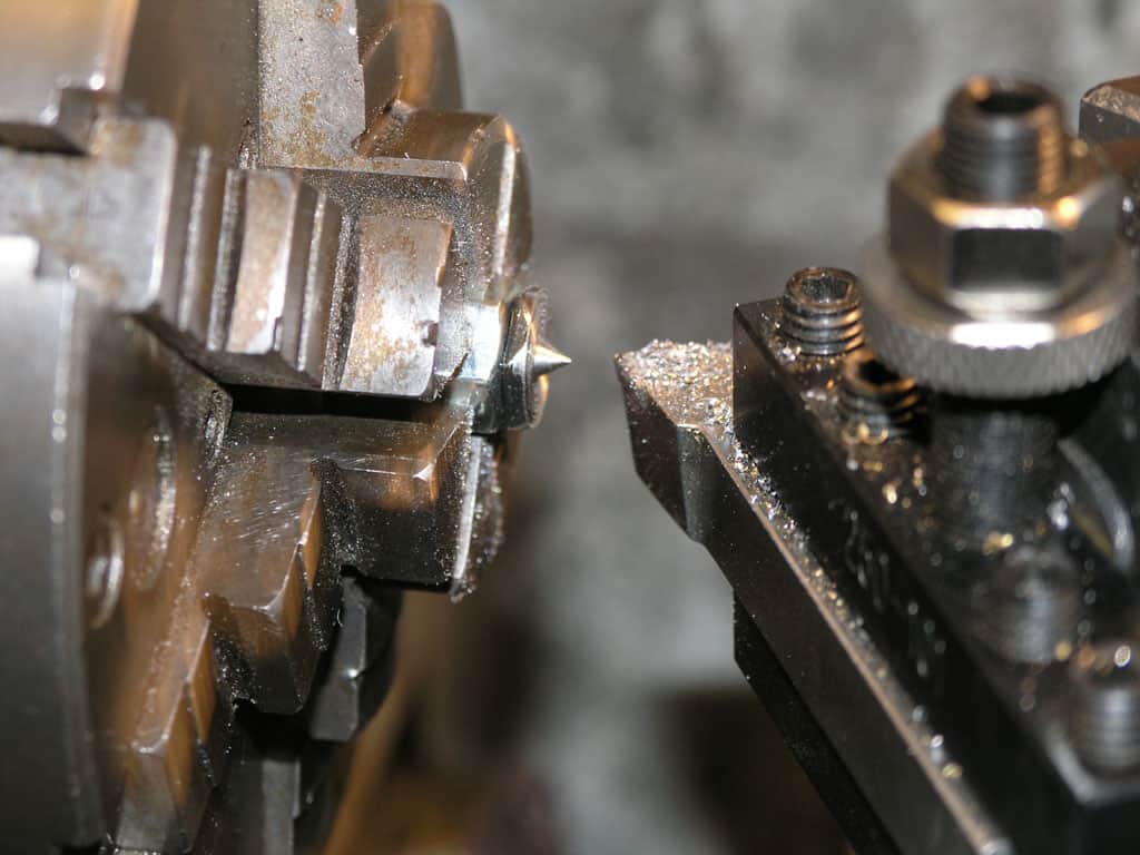 Metal cutting tool with pointed tip and metal shavings nearby.