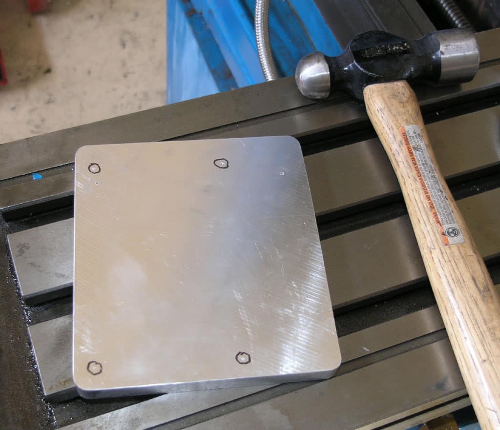 Metal sheet on workbench with hammer handle, aluminum or stainless steel with circular indents.