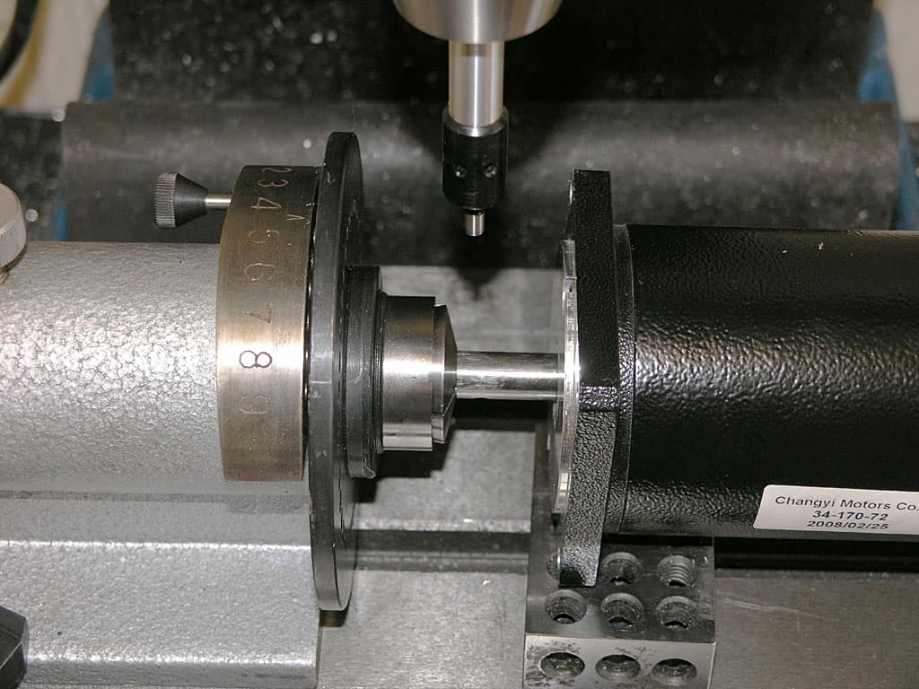 A close-up photograph of a machine spindle with black cylindrical component and silver rod protruding from it.