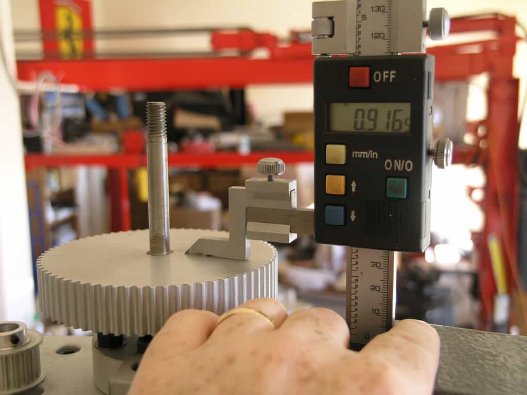 Digital caliper with LCD display on black body, measuring metal rod.