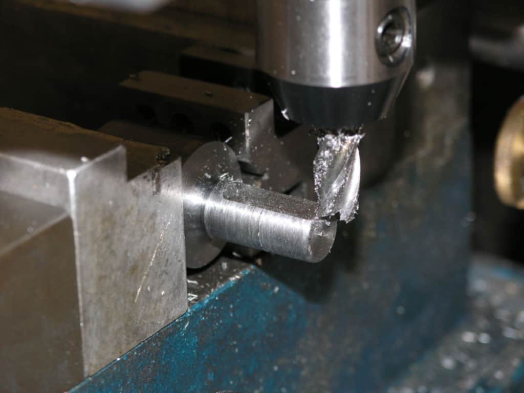 Metal workpiece being machined on a vertical milling machine or CNC lathe, with metal shavings and chips.